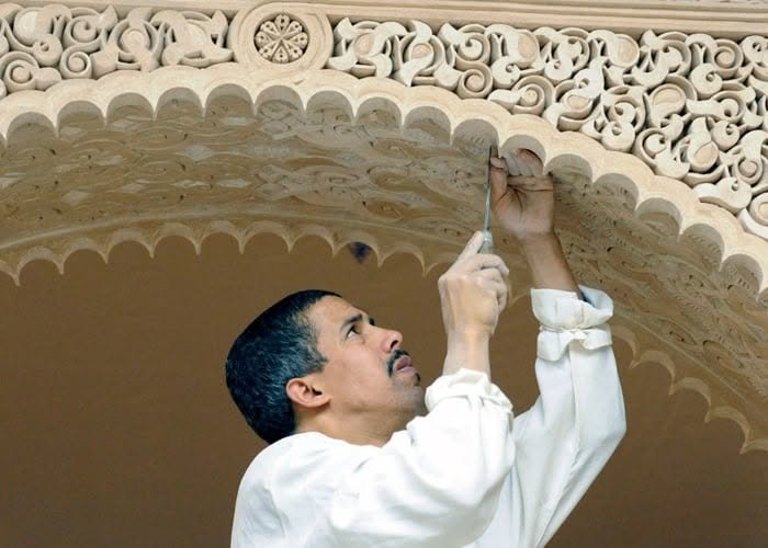 Artisan marocain sculptant à la main les motifs d’une arche en plâtre